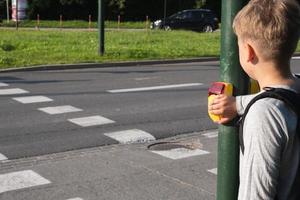 Schuljunge in der Nähe von Fußgängerüberweg und drückt bei Bedarf gelbes Gerät mit Knopf an der Ampel foto