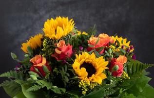 Nahaufnahme eines bunten, frischen Blumenstraußes aus Rosen und Sonnenblumen, vor einem grauen Hintergrund foto