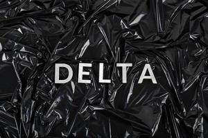 das wort delta mit silbernen metallbuchstaben auf zerknittertem schwarzem plastiktütenhintergrund foto