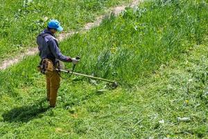 tula, russland 19. mai 2020 russischer offizieller rasenmäher-arbeiter, der grünes gras mit zweitaktmotor-saitenschneider schneidet. Ansicht von oben nach unten. foto