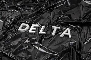 das wort delta mit silbernen metallbuchstaben auf zerknittertem schwarzem plastiktütenhintergrund in diagonaler perspektive foto