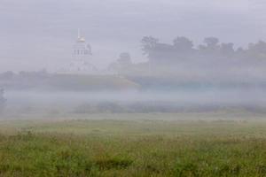 Nebelige Sommermorgenlandschaft mit der Kirche auf dem Hügel im Hintergrund foto