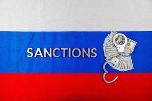 das wort sanktionen mit silbernen metallbuchstaben auf der russischen trikolore in der nähe von dollarbanknoten und handschellen direkt über der ansicht foto