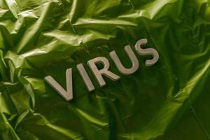Das Wort Virus mit silbernen Metallbuchstaben auf zerknitterter grüner Kunststofffolie mit dramatischem Licht foto