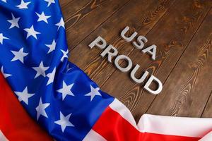 worte usa stolz mit silbernen metallbuchstaben auf brauner holzoberfläche mit flagge der vereinigten staaten von amerika gelegt foto