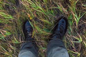 Füße in nassen schwarzen Armeestiefeln und grünen Baumwollhosen im Herbstgras Gonzo nach unten. foto