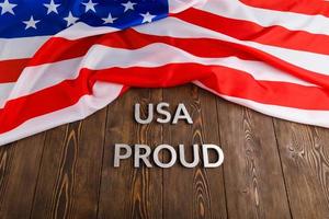worte usa stolz mit silbernen metallbuchstaben auf brauner holzoberfläche mit flagge der vereinigten staaten von amerika gelegt foto