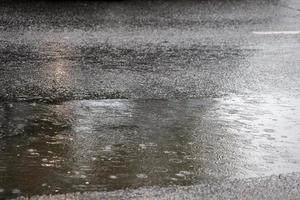 Pfütze auf Asphaltstraße bei Regen in der Stadt mit selektivem Fokus und Boke-Unschärfe foto