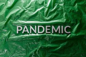 das Wort Pandemie mit silbernen Buchstaben auf grünem, zerknittertem Kunststofffolienhintergrund in flacher Laienzusammensetzung in der Mitte foto