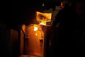 Arbeiter, der Schlacke aus dem metallurgischen Ofen mit Abzugshaube entfernt und Metall mit Dampf schmilzt foto