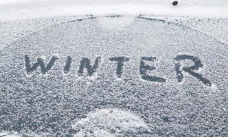 Wort Winter handschriftlich auf schneebedecktes Autofenster im Wintermorgenlicht foto