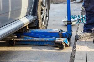 silbernes ziviles Autoheben mit altem hydraulischen Wagenheber in einer Autowerkstatt im Freien. Wechselverfahren für Saisonreifen. foto