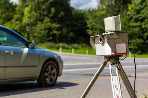 Mobiles Blitzergerät, das tagsüber auf Sommerstraßen mit verschwommenem silbernem Auto im Hintergrund arbeitet foto