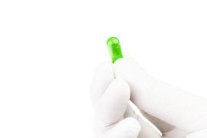 Hand im medizinischen Handschuh, der UFO-grüne organische med-Kapsel hält, die auf weißer Hintergrundnahaufnahme lokalisiert wird foto