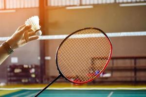 Badmintonspieler hält Schläger und Federball mit weißer Creme vor das Netz, bevor er ihn auf einer anderen Seite des Platzes serviert. foto