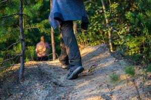 Wandermannbeine mit Schuhen und Hosen irgendwo im Sommerwald, Nahaufnahme mit selektivem Fokus. verschwommene Mädchensilhouette im Hintergrund. foto