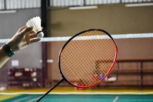 Badmintonspieler hält Schläger und Federball mit weißer Creme vor das Netz, bevor er ihn auf einer anderen Seite des Platzes serviert. foto