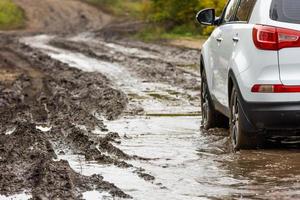 sauberes weißes suv-auto, das sich auf einer unbefestigten straße mit nassem lehm vor einem verschwommenen hang bewegt foto