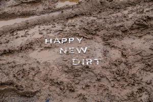 die worte happy new dirt legten sich mit silbernen metallbuchstaben auf die nasse schlammoberfläche foto