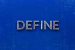 das wort "define" auf blau lackiertem karton mit dicken großbuchstaben aus silbermetall foto