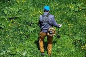 Rasenmäher-Arbeiter, der grünes Gras mit Zweitaktmotor-Schneidrimmer in Russland schneidet. foto