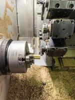 CNC-Drehmaschine mit vielen Messingspänen im Inneren beim Drehen des sechseckigen gelben Metallstangenwerkstücks foto