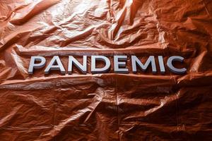 das Wort Pandemie mit silbernen Buchstaben auf rotem, zerknittertem Kunststofffolienhintergrund. schräge Perspektive. foto