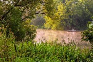 tula, russland 12. august 2013 ein mann, der am nebligen sommermorgen unter grünem laub am fluss am schlauchboot fischt. foto