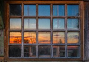 schmutziges Holzfenster mit Reflexion des Sonnenunterganghimmels foto