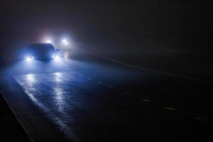 Zwei verschwommene Autos, die sich auf einer leeren, nächtlichen, nebligen Straße bewegen foto