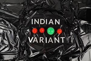 Wörter indische Variante mit silbernen Metallbuchstaben auf zerknittertem schwarzem Plastiktütenhintergrund mit kleinen Virusmodellen foto