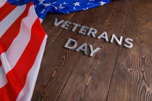 die worte veterans day legten mit silbernen metallbuchstaben auf holzbrettoberfläche mit zerknitterter usa-flagge foto
