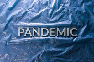 das Wort Pandemie mit silbernen Buchstaben auf zerknittertem blauem Kunststofffolienhintergrund in flacher Laienzusammensetzung in der Mitte foto