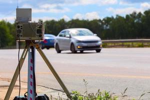 mobiles Blitzergerät, das tagsüber auf Sommerstraßen mit verschwommenem weißem Auto im Hintergrund arbeitet foto