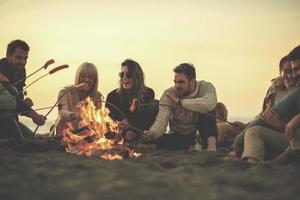 Gruppe junger Freunde, die am Feuer am Strand sitzen foto