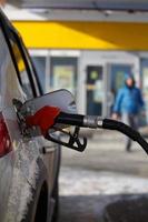 Silberfarbenes Auto, das an einer Tankstelle im Winter tankt - Nahaufnahme mit selektivem Fokus und verschwommener Mannsilhouette im Hintergrund foto