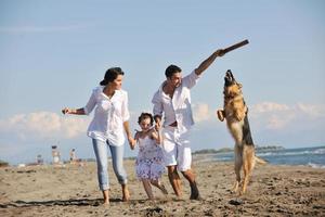 glückliche familie, die mit hund am strand spielt foto