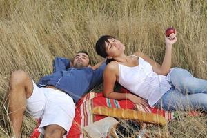 glückliches Paar, das ein Picknick auf dem Land im langen Gras genießt foto