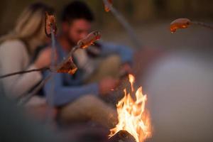 Gruppe junger Freunde, die am Feuer am Strand sitzen foto