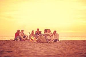 Gruppe junger Freunde, die am Feuer am Strand sitzen foto