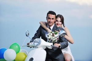 Gerade verheiratetes Paar am Strand fährt weißen Roller foto
