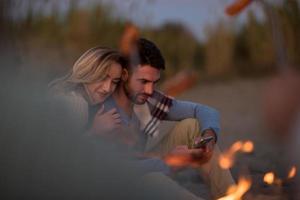 Gruppe junger Freunde, die am Feuer am Strand sitzen foto