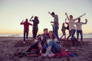 Paar genießt mit Freunden den Sonnenuntergang am Strand foto