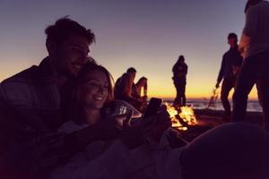 Paar genießt Lagerfeuer mit Freunden am Strand foto