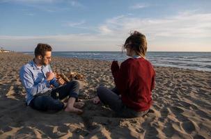 junges Paar sitzt am Strand neben Lagerfeuer und trinkt Bier foto