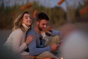 Gruppe junger Freunde, die am Feuer am Strand sitzen foto