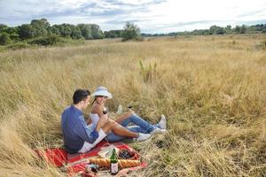 glückliches Paar, das ein Picknick auf dem Land im langen Gras genießt foto