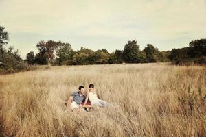 glückliches Paar, das ein Picknick auf dem Land im langen Gras genießt foto