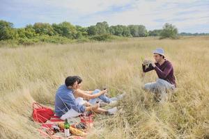 glückliches Paar, das ein Picknick auf dem Land im langen Gras genießt foto