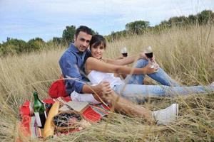 glückliches Paar, das ein Picknick auf dem Land im langen Gras genießt foto